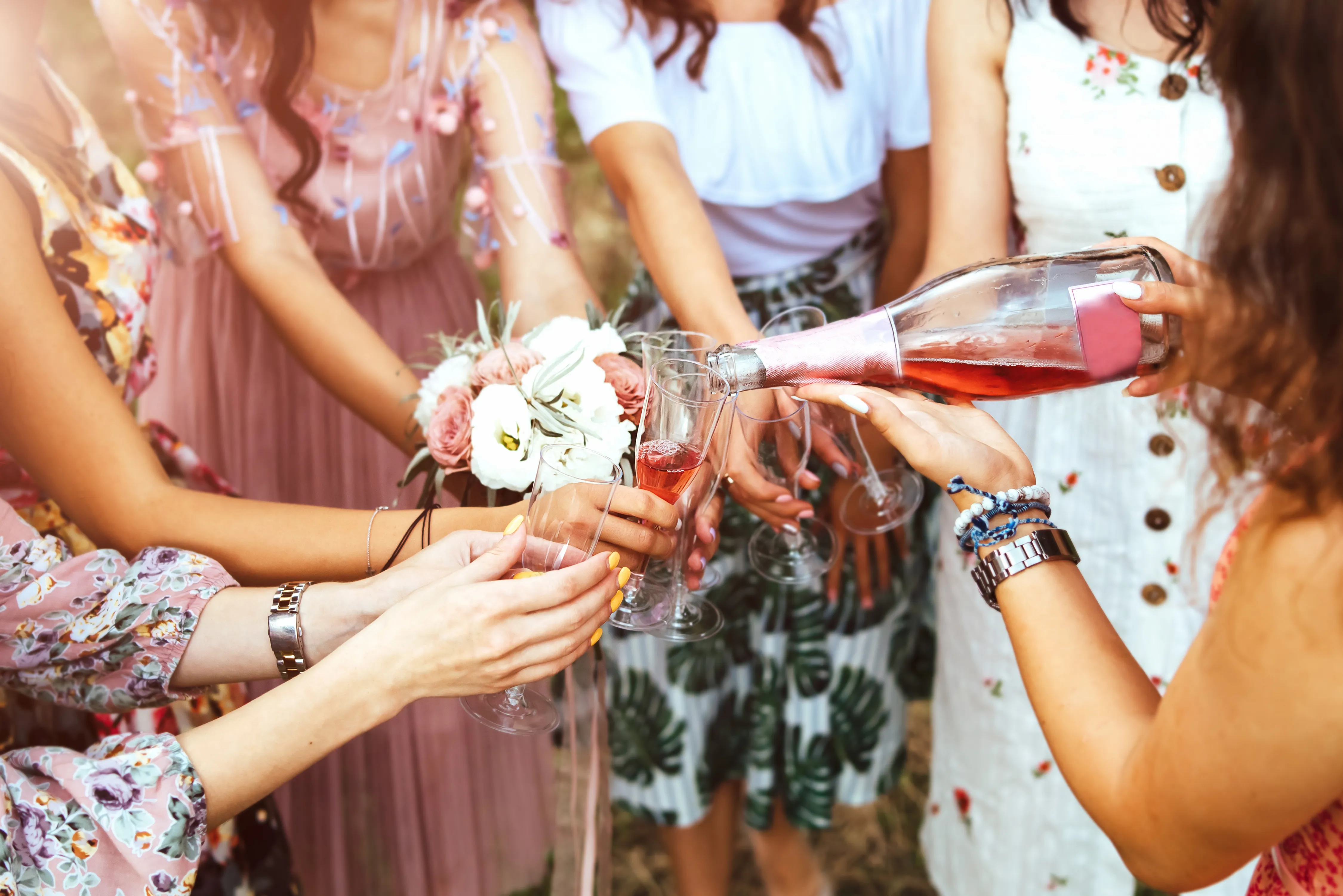 Friends in floral dresses pouring rosé over champagne flutes in golden light