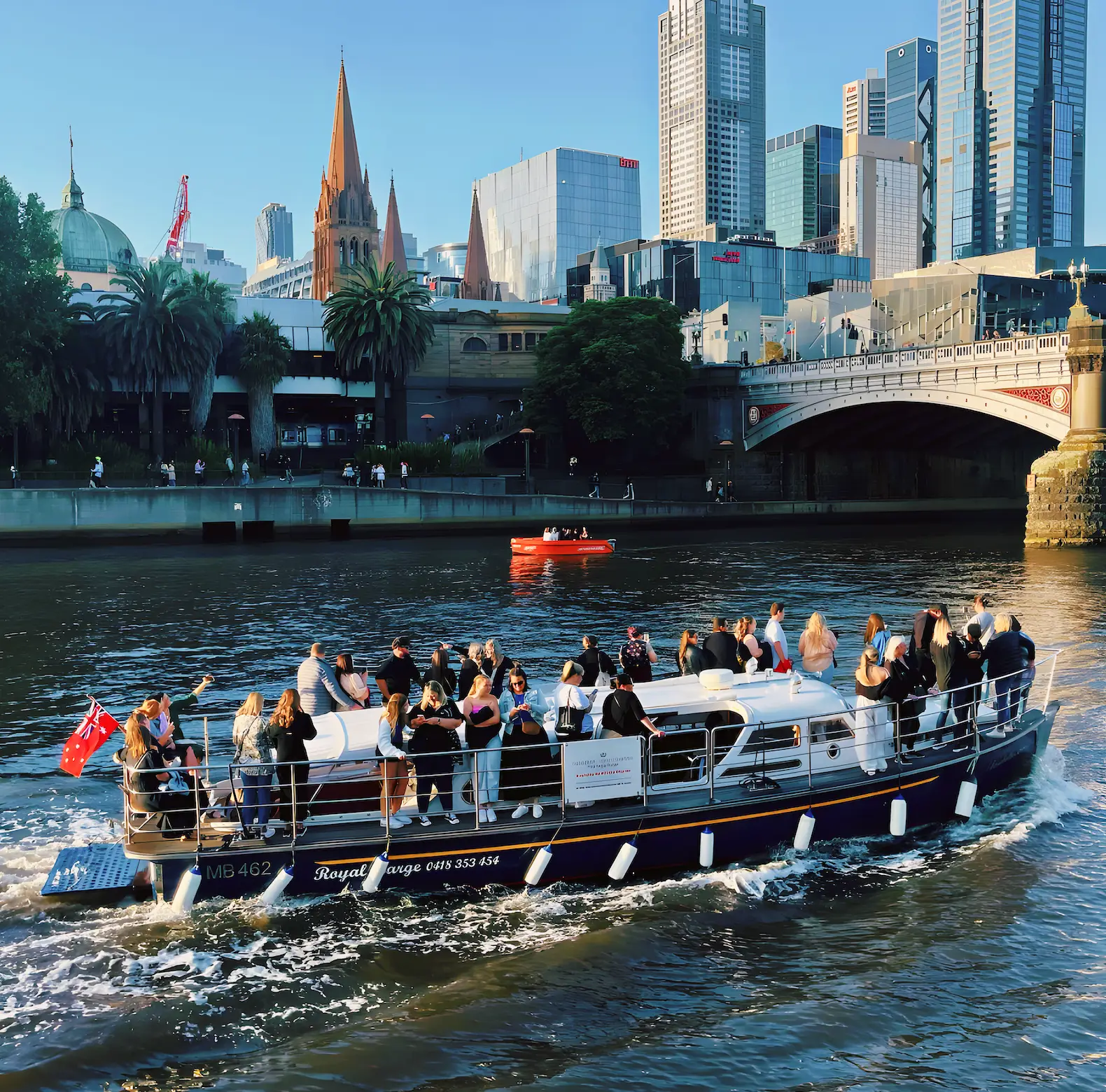 Elizabeth Anne cruising the Yarra past Princes Bridge with guests aboard, Melbourne skyline behind