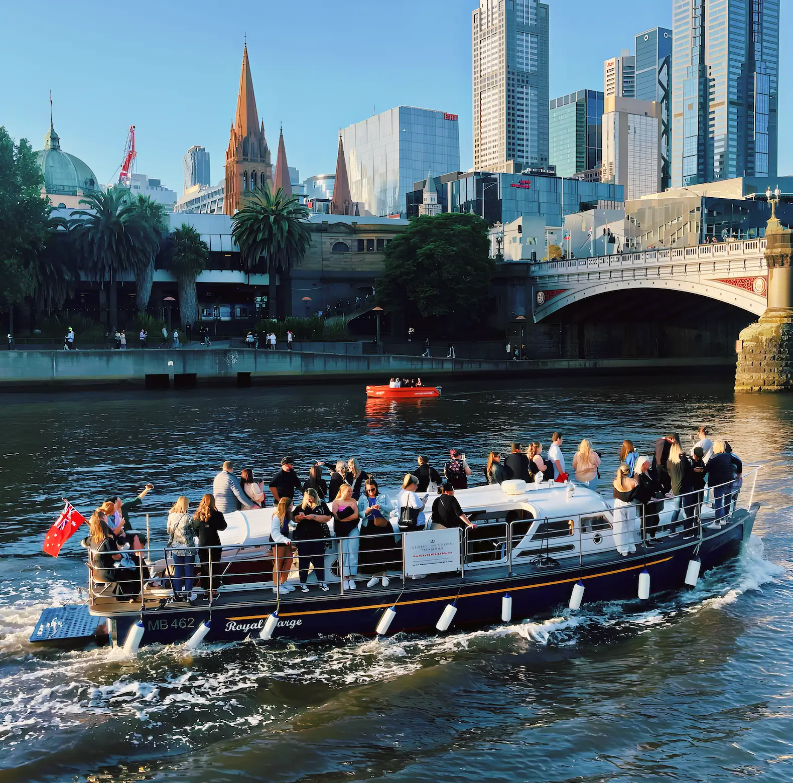 Elizabeth Anne cruising the Yarra past Princes Bridge with guests aboard, Melbourne skyline behind