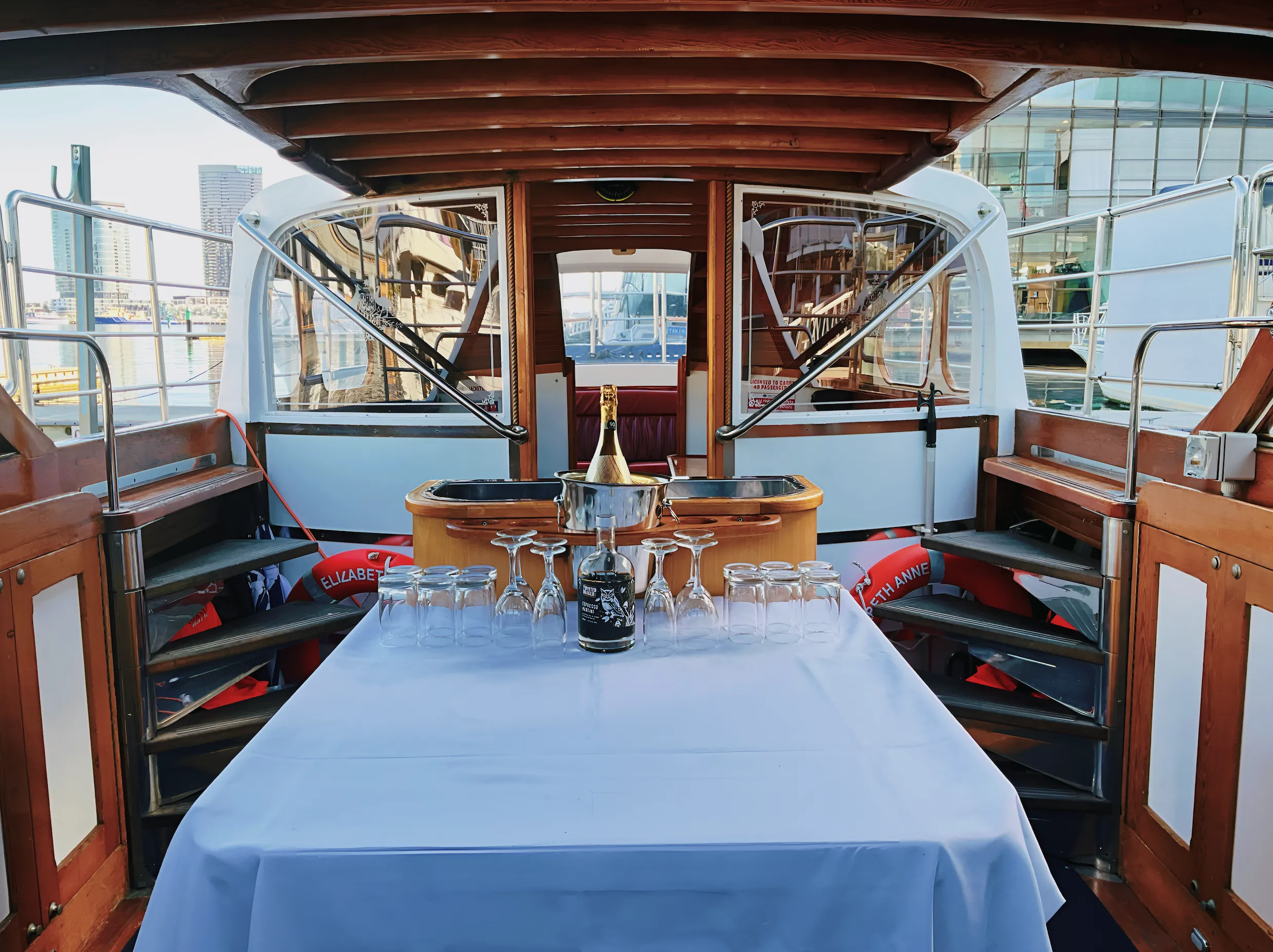 The stern deck set with a white-clothed table, glassware and a champagne bucket in marina light